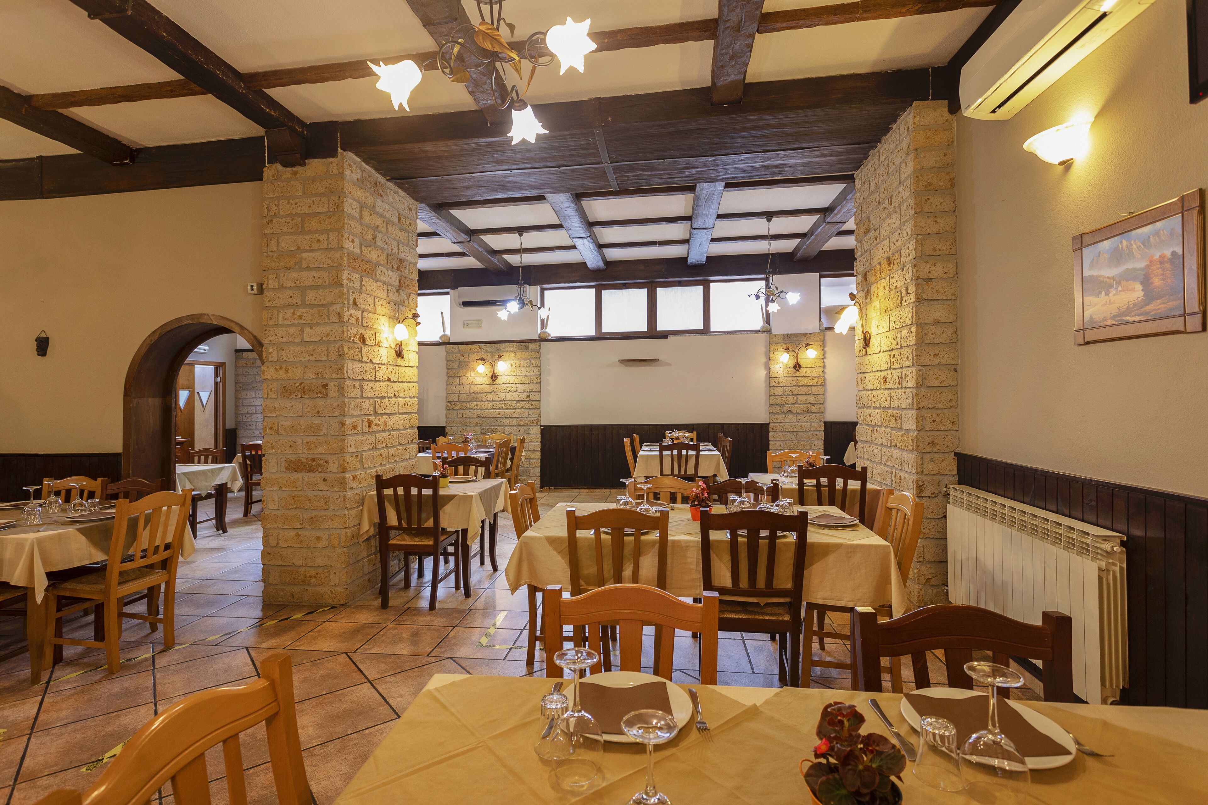 A restaurant with stone walls, wooden beams, and tables set for dining.