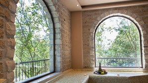 Una habitación con pared de piedra, ventana con vistas a árboles y una zona con bancos de cerámica.