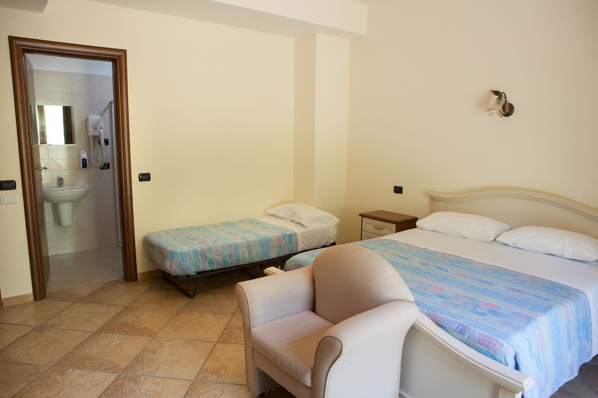 Un dormitorio con dos camas individuales, una silla, una mesita de noche y un baño visible a través de una puerta abierta.