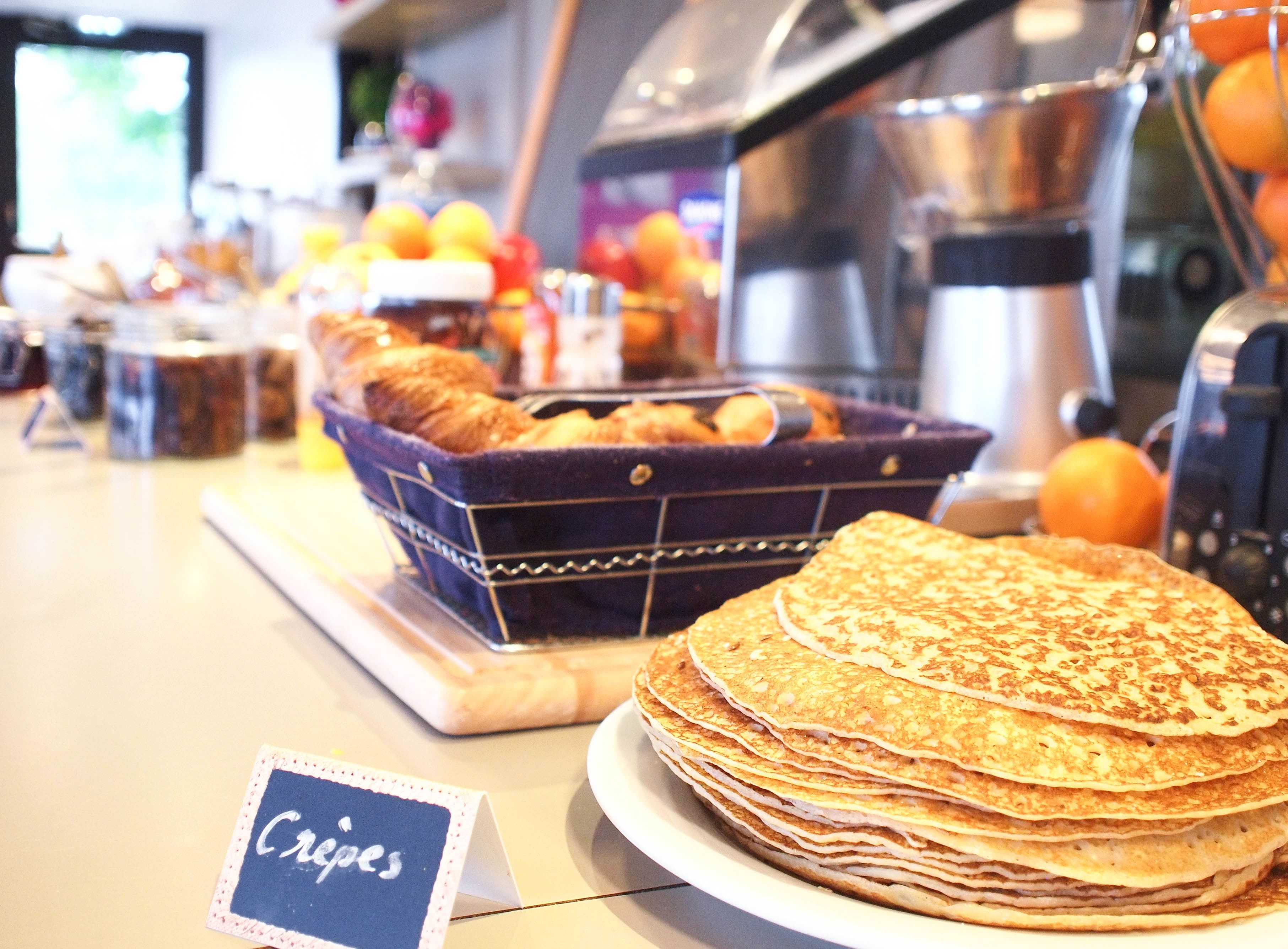A breakfast buffet with a sign for crepes, a basket of pastries, and a stack of crepes on a plate.