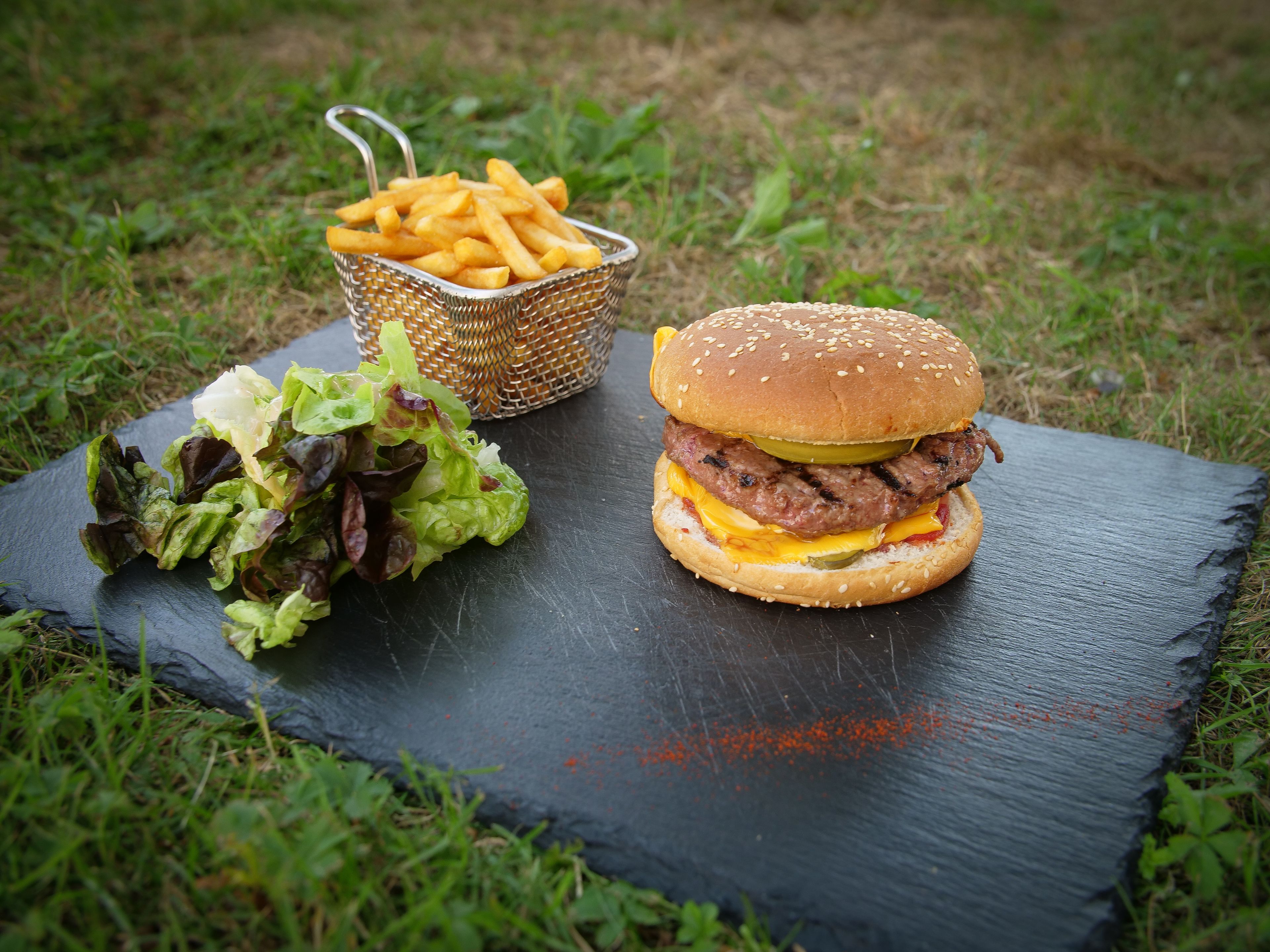 Hamburguesa con lechuga, queso y pan, acompañada de papas fritas y una ensalada en una tabla de pizarra.