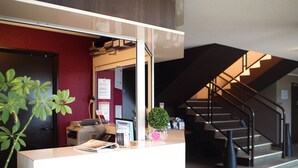 A reception desk with a computer, a small plant, and a red wall in the background. - Hôtel Inn Design & Restaurant Le Mans (Arnage)