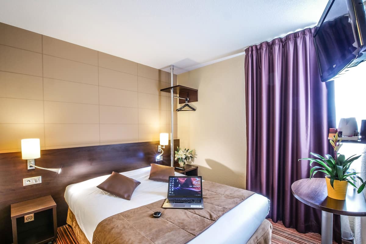 A hotel room with a bed, bedside table, lamp, laptop, and a small table with a plant.