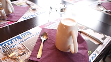 Una mesa con una taza de café, una cuchara y un menú sobre un servilleta morada.