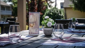 A table set for dining with a menu, a potted plant with white flowers, and empty wine glasses. - Hôtel Inn Design & Restaurant Le Mans (Arnage)