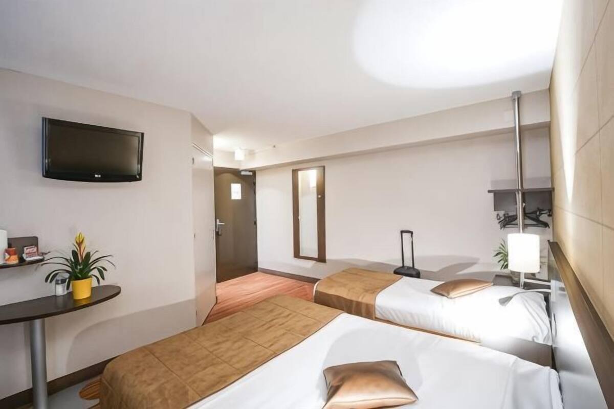 A hotel room with two beds, a desk, a TV, and a plant.