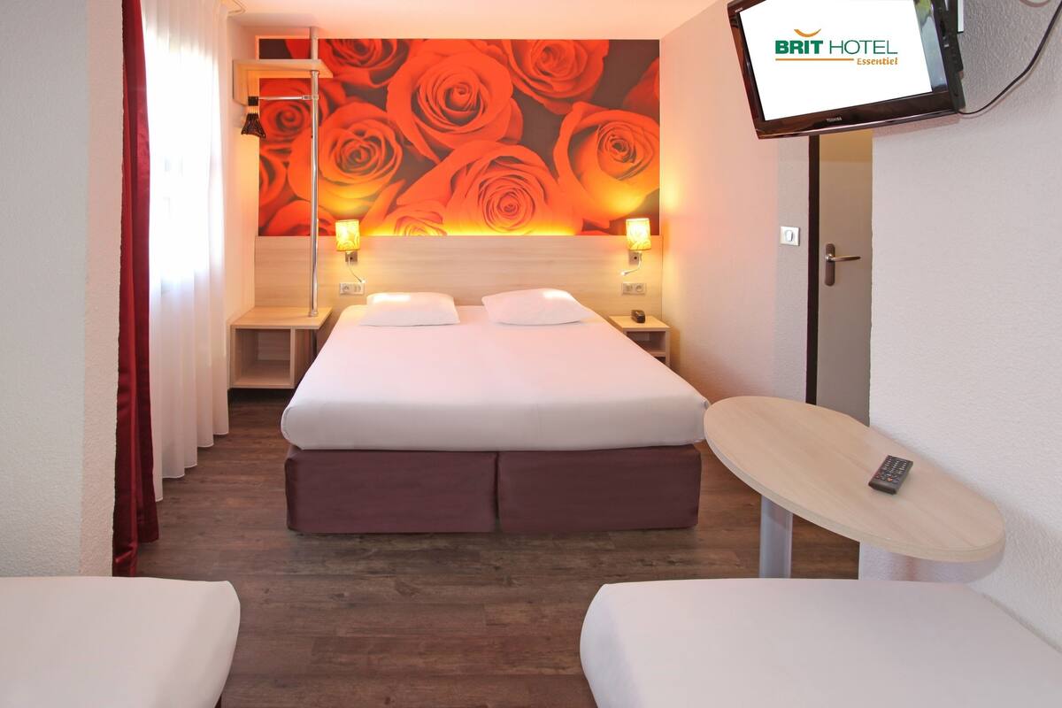 Une chambre d’hôtel avec un grand lit, deux tables de chevet, un téléviseur fixé au mur et une petite table avec une télécommande.