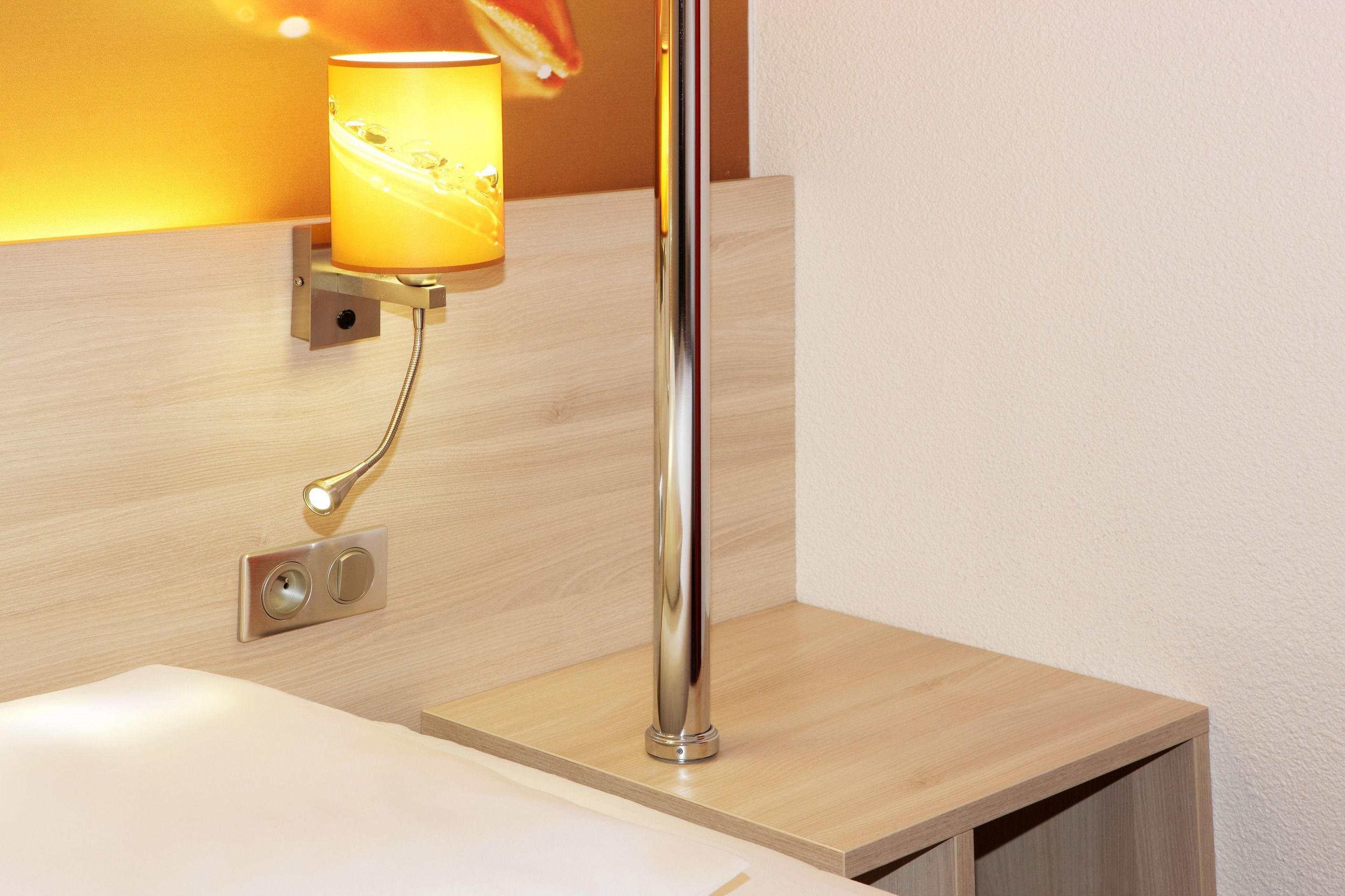 A modern bathroom with a wooden vanity, a chrome faucet, and a wall-mounted lamp.