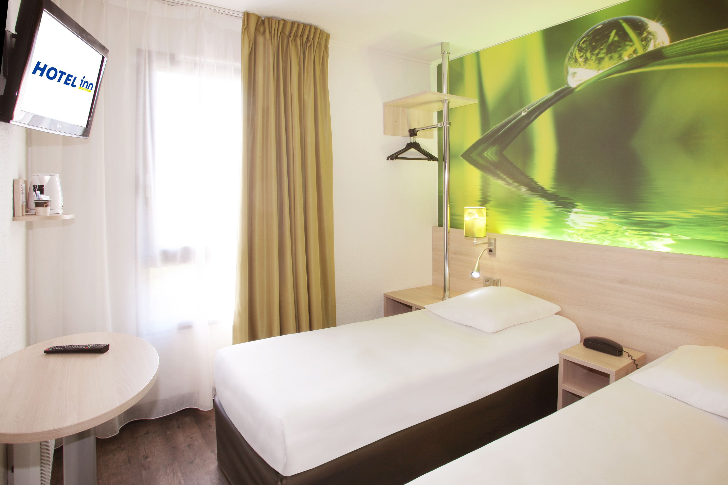 Una habitación de hotel con cama, mesita de noche, lámpara y televisor mostrando 'HOTEL INN'.