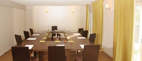 Un salón de conferencias con una larga mesa, sillas y un ventanal con cortinas.