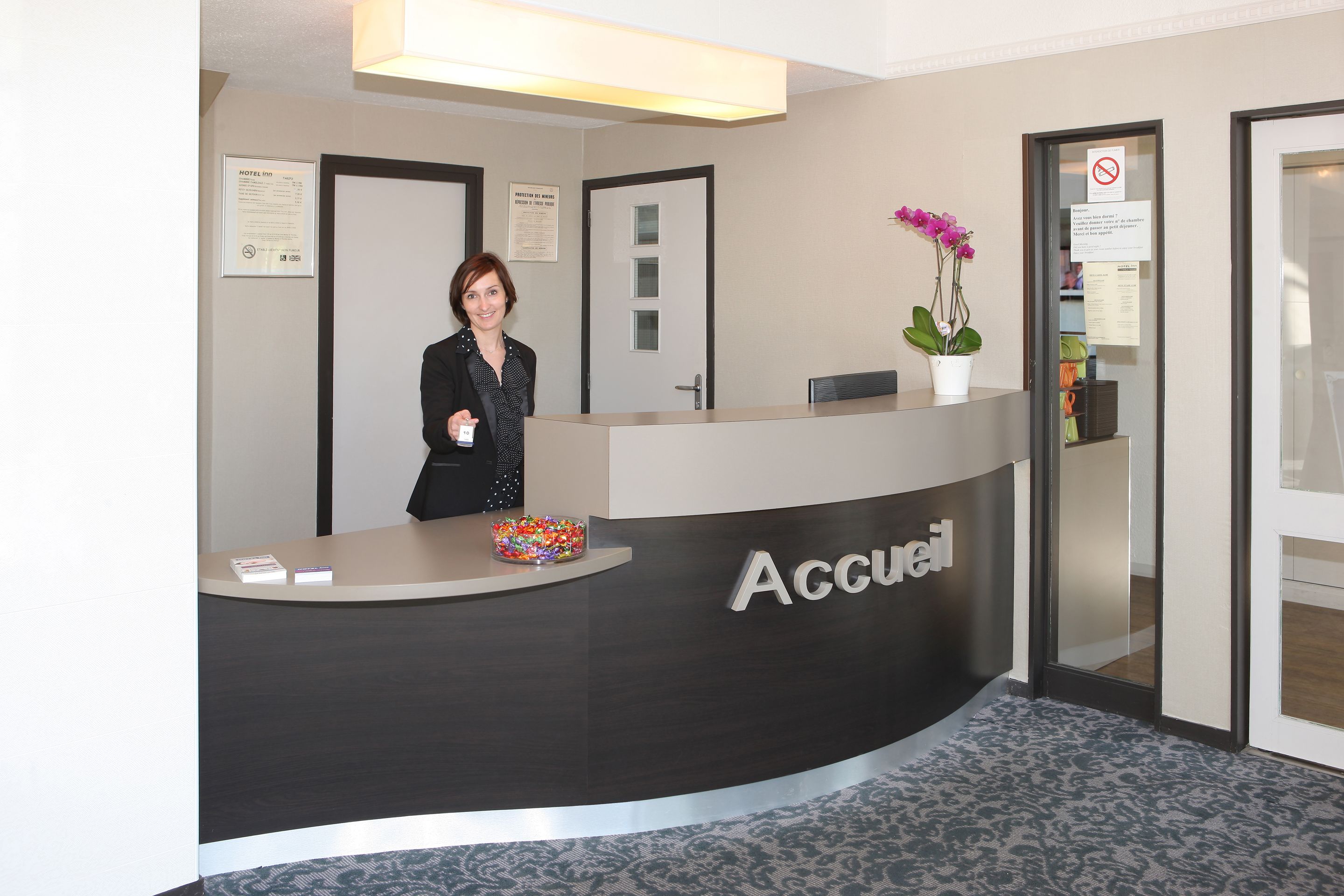 Una mesa de recepción con un cartel que dice 'Accueil' y una mujer de pie detrás.