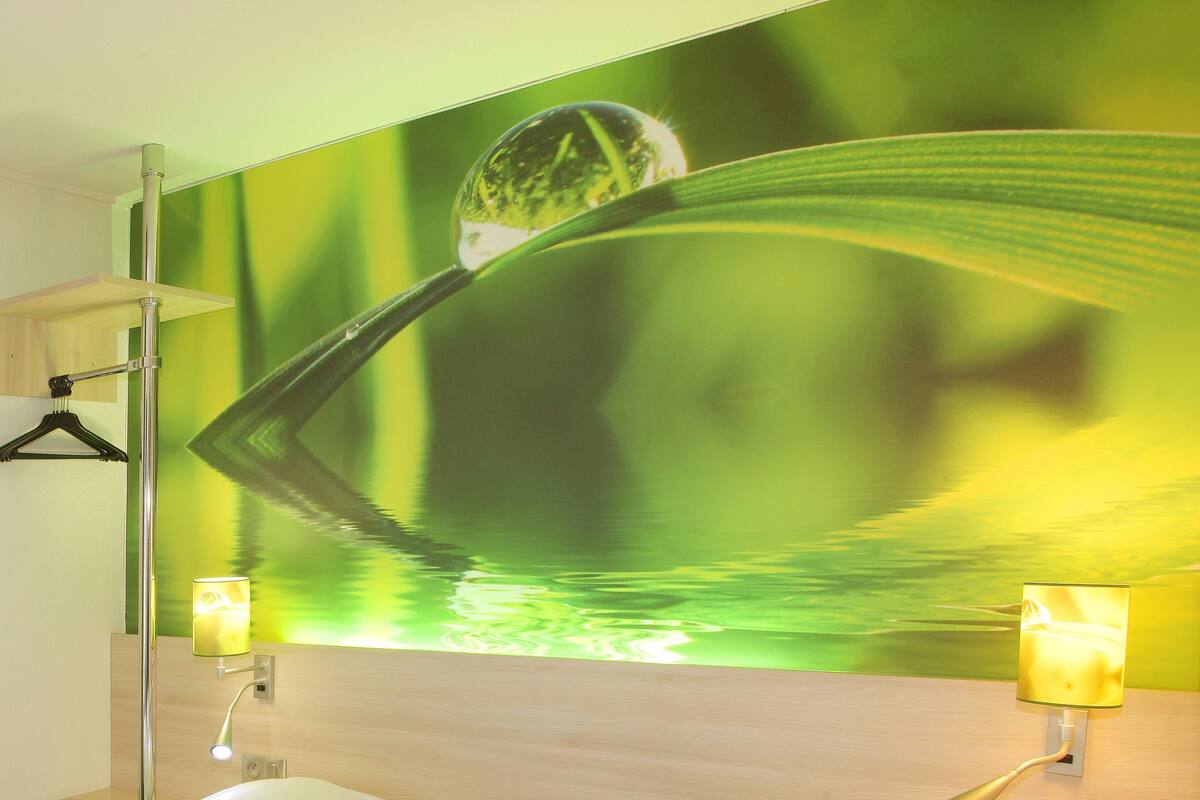 Une salle de bain avec un mur vert, un miroir et deux lampes fixées au mur.