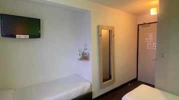 A hotel room with two single beds, a flat-screen TV mounted on the wall, a mirror, and a door with a light switch.