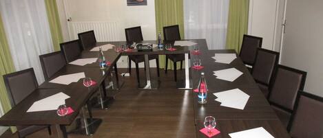Un salón de conferencias con una larga mesa, sillas y un proyector.