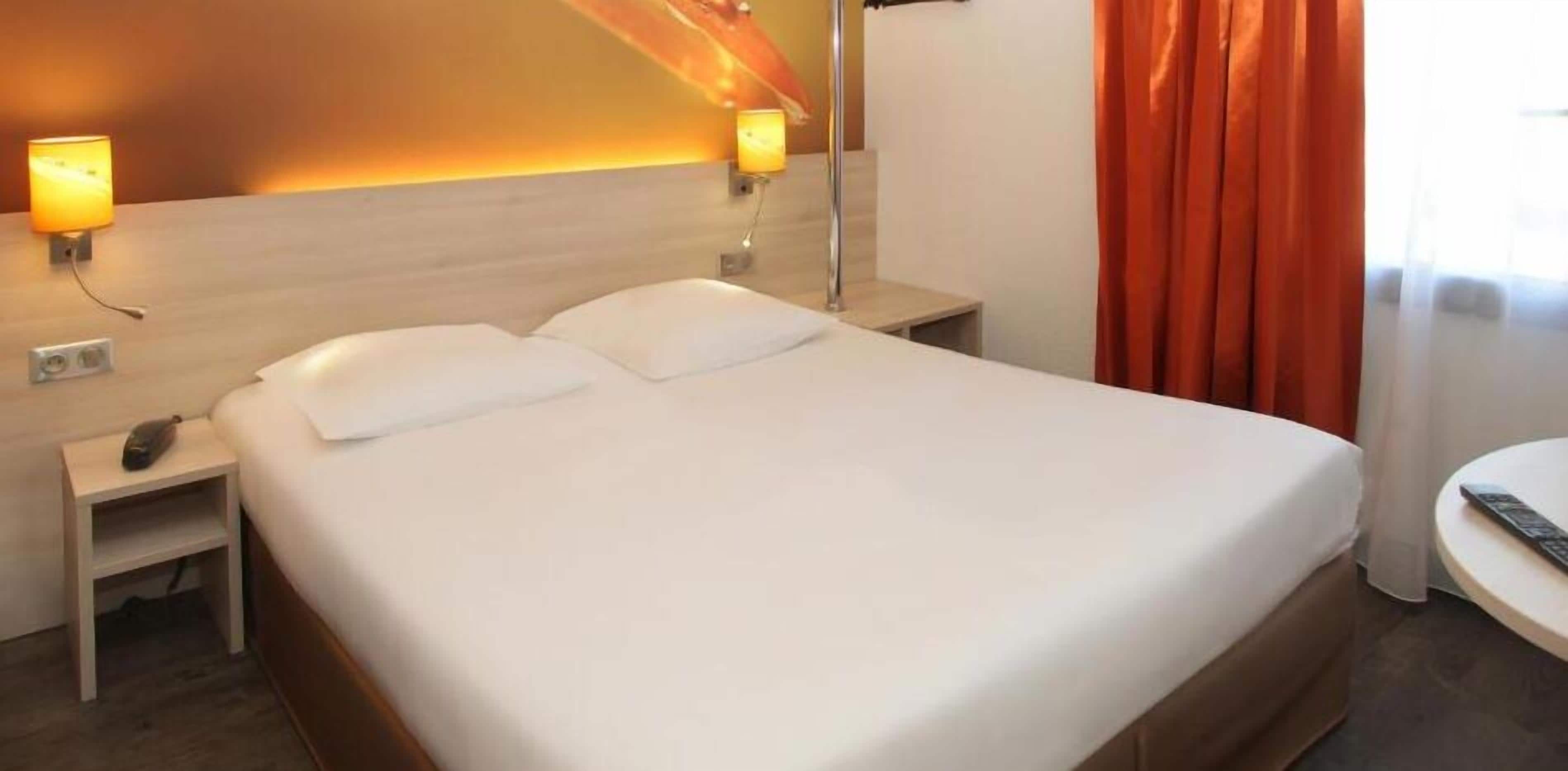 Une chambre d’hôtel avec un grand lit, deux tables de chevet, une lampe et une petite table sur laquelle se trouve une télécommande.