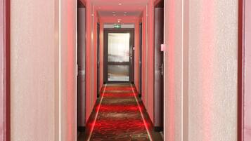 A hotel hallway with a red carpet and a glass door at the end.