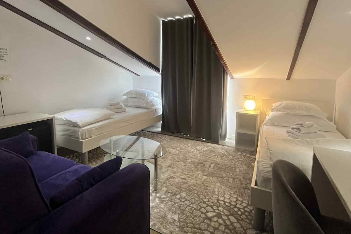 A compact hotel room with a bed, a small desk, a purple sofa, and a glass coffee table.