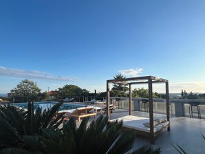 Un espace piscine aménagé sur le toit, avec des chaises longues, une pergola en bois et une vue sur le paysage environnant.