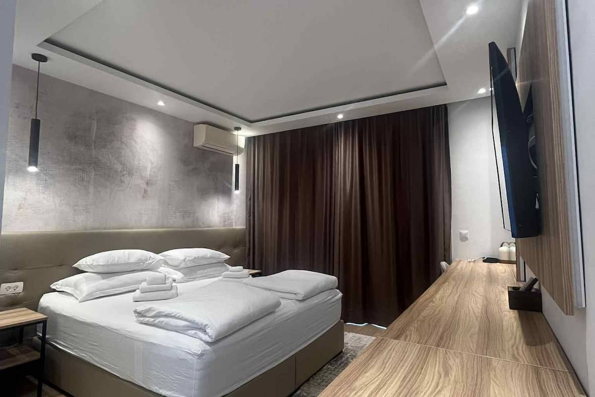 A modern bedroom with a large bed, a flat-screen TV mounted on the wall, and a wooden floor.