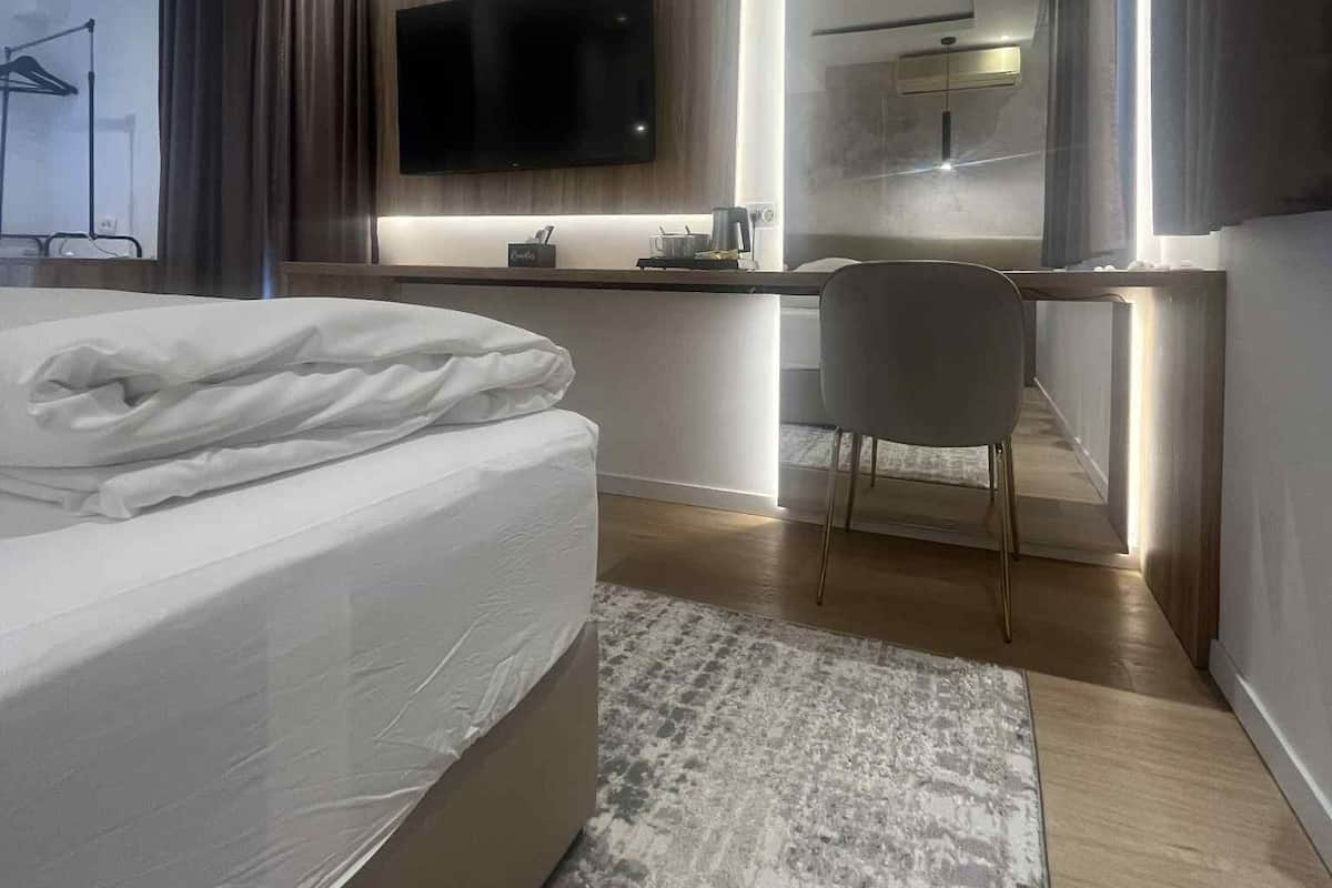 A modern bedroom with a large bed, a desk, and a flat-screen TV.