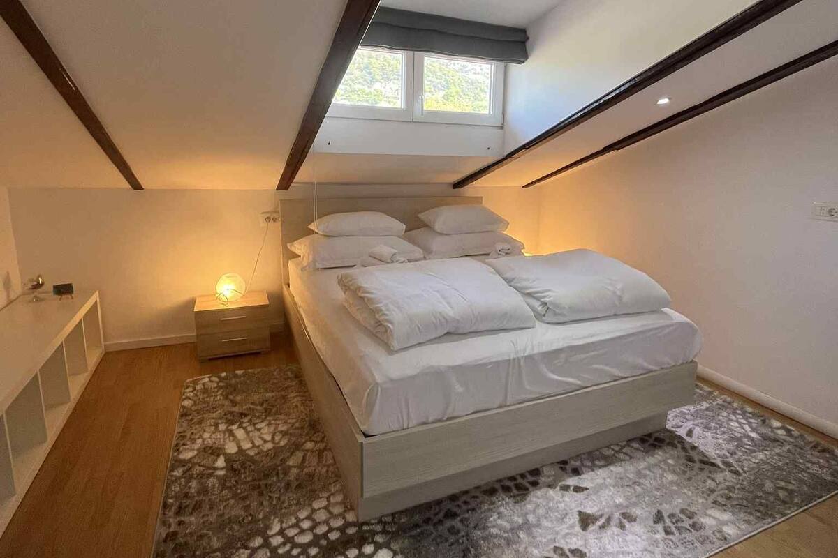 A bedroom with a bed, a nightstand, a window, and a ceiling light.