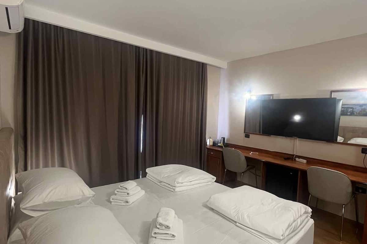 A hotel room with a bed, a desk, a chair, a television, and a window with curtains.
