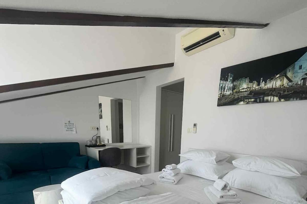 A hotel room with a large bed, a blue sofa, a desk with a mirror, and a painting on the wall.