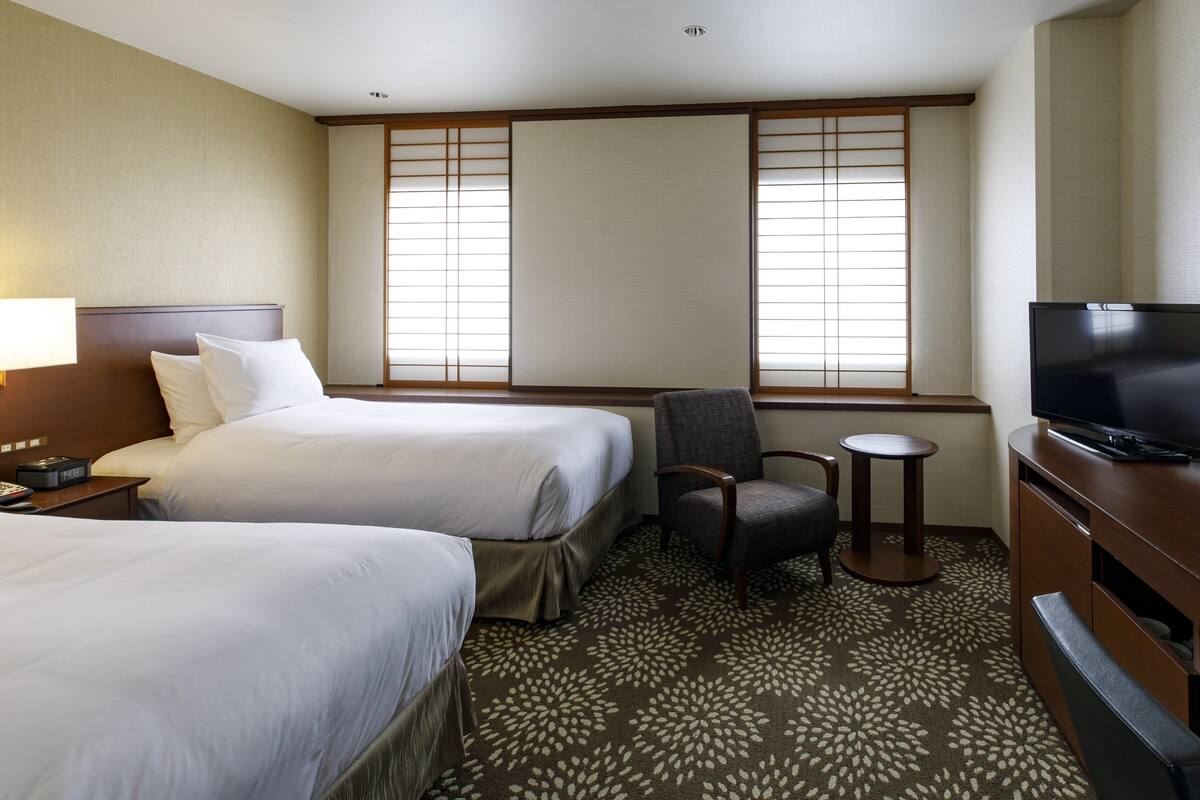 A hotel room with two beds, a TV, a chair, and a small table.