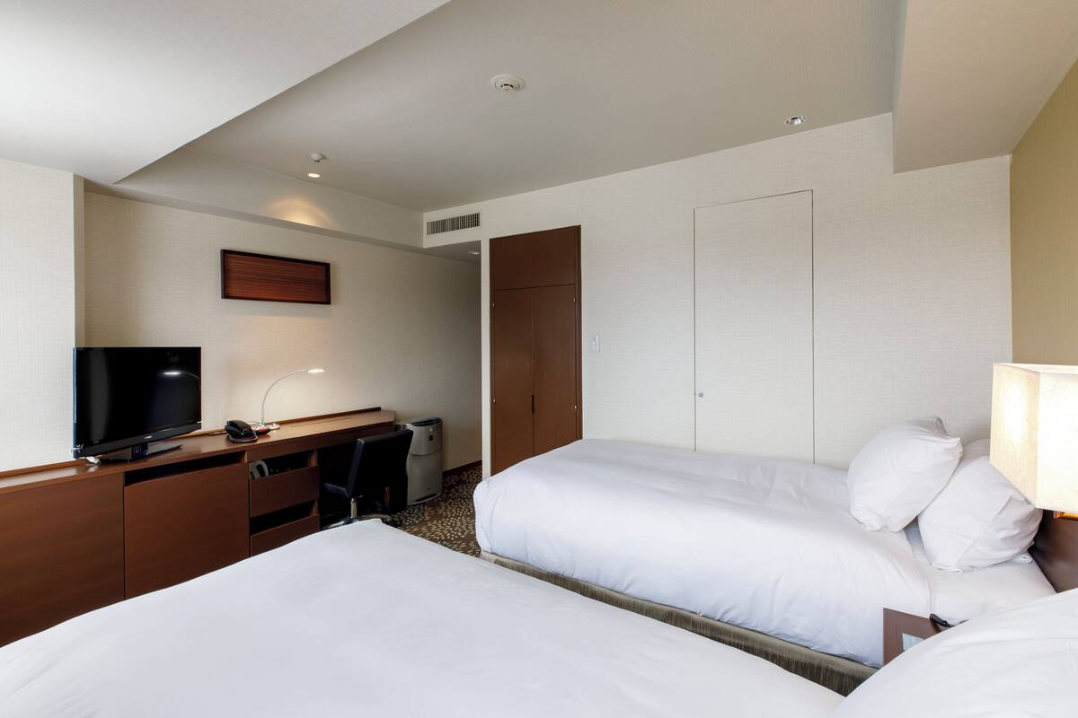 A hotel room with two beds, a desk with a television, and a wardrobe.