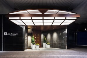 The entrance of ANA Holiday Inn with a modern design, featuring a large illuminated canopy, a reception desk, and potted plants. - Holiday Inn ANA Kanazawa Sky by IHG (Kanazawa)