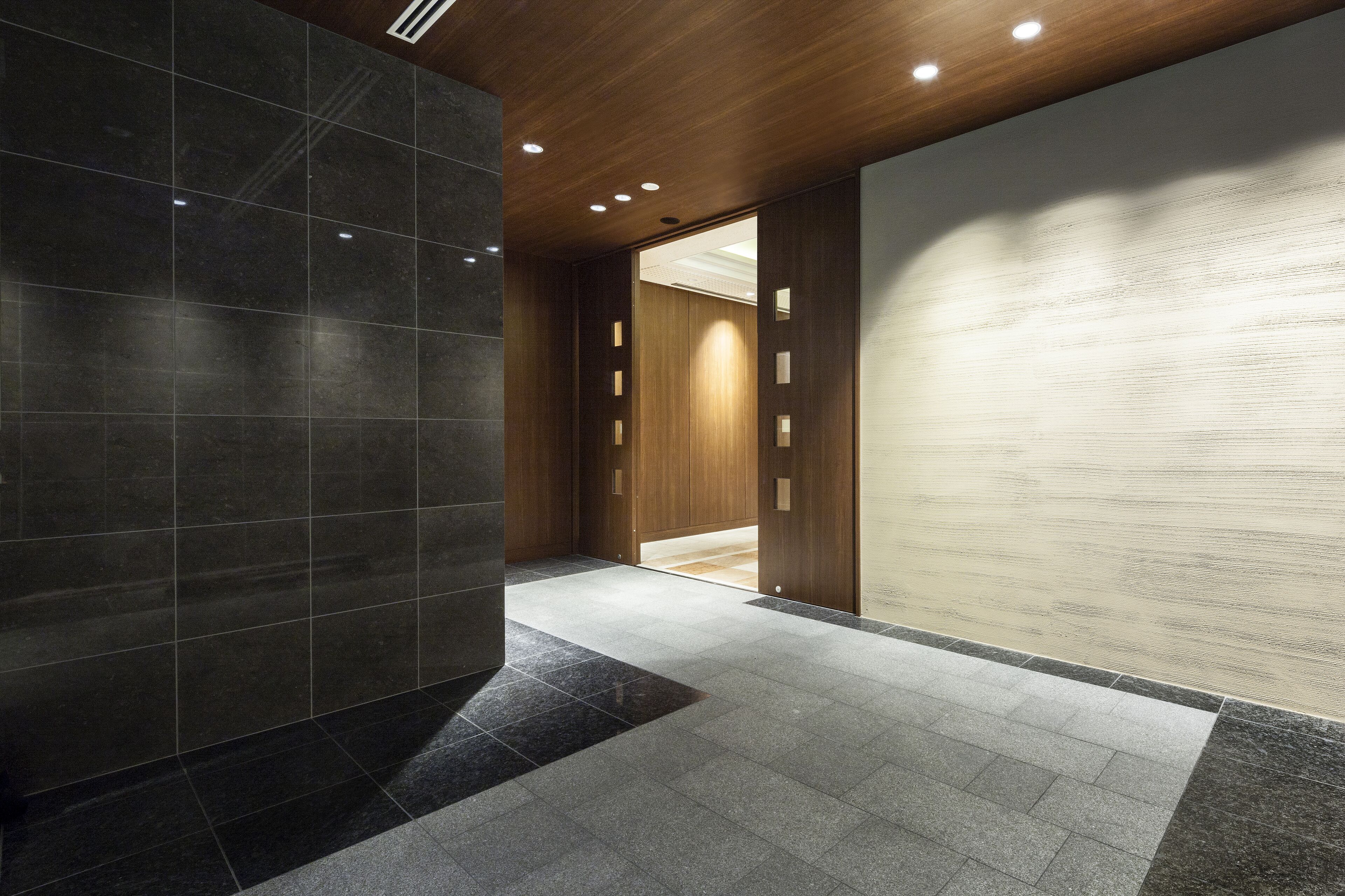 A modern hallway with dark tiled walls, a wooden ceiling, and recessed lighting.