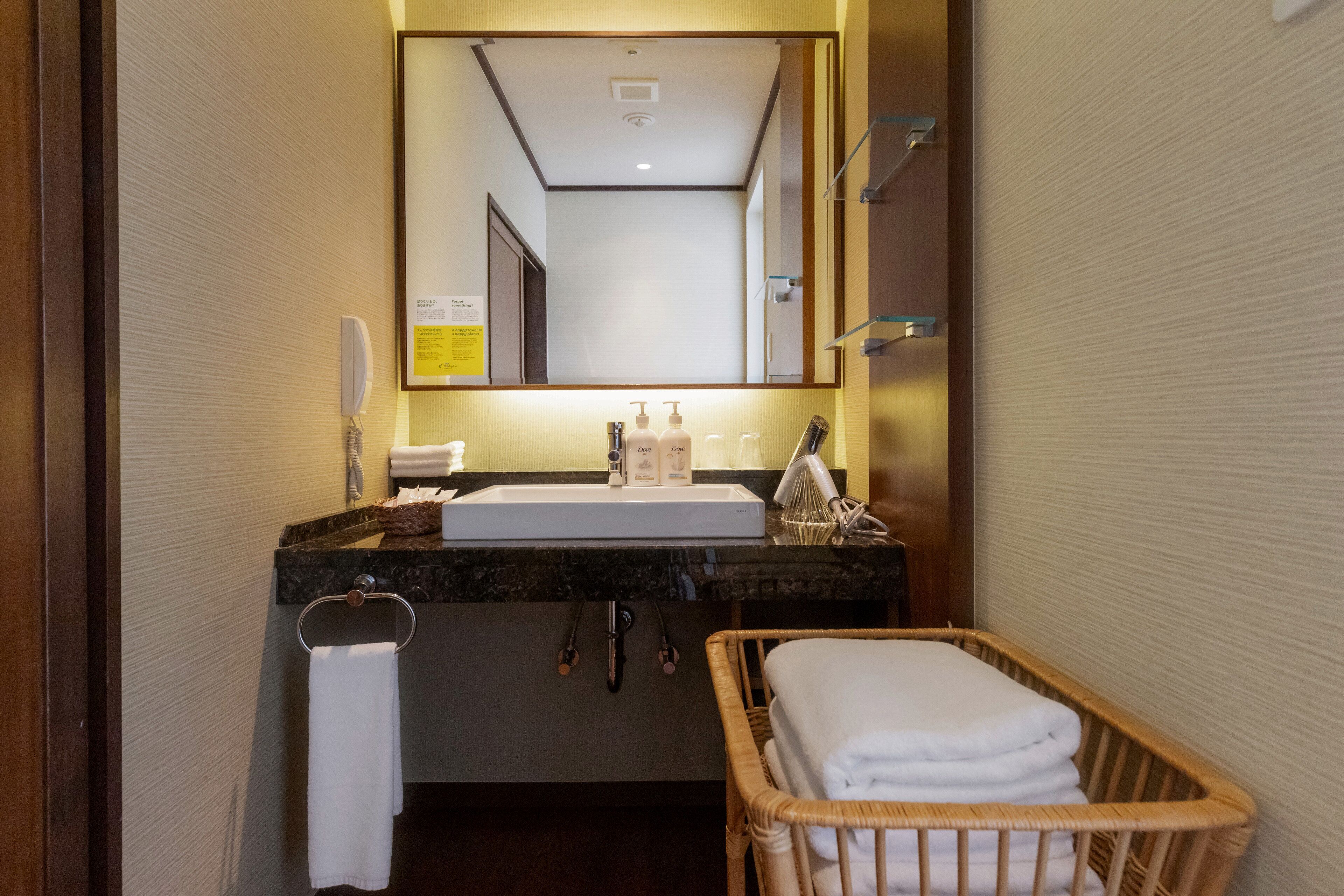 A hotel bathroom with a sink, mirror, towel rack, and a wicker basket with towels.