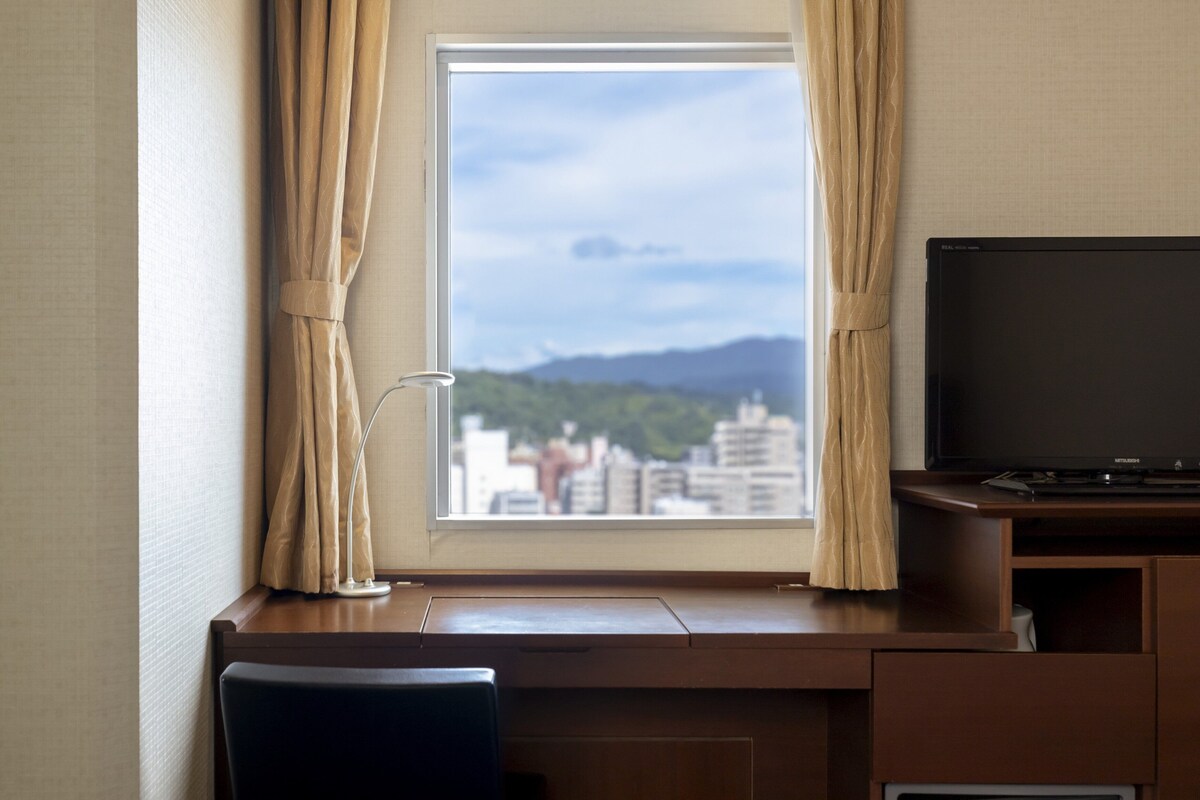 Habitación de hotel con escritorio, silla, televisor y ventana con cortinas.