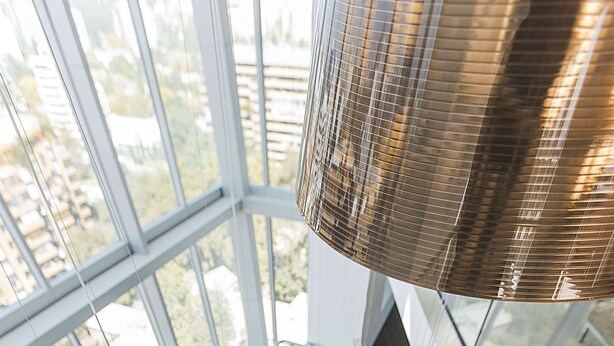 Un interior moderno con una escalera de cristal, barandillas de metal y lámparas colgantes esféricas.