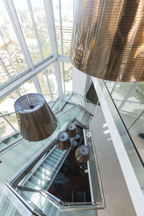 Un interior moderno con una escalera de cristal, barandillas de metal y lámparas colgantes esféricas.