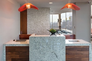 A modern kitchen with granite countertops, wooden cabinets, and two pendant lights.