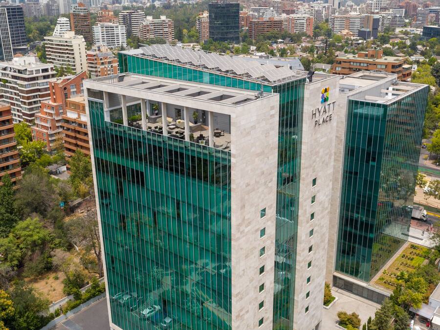 A modern hotel with a glass facade, multiple floors, and a rooftop terrace with solar panels.
