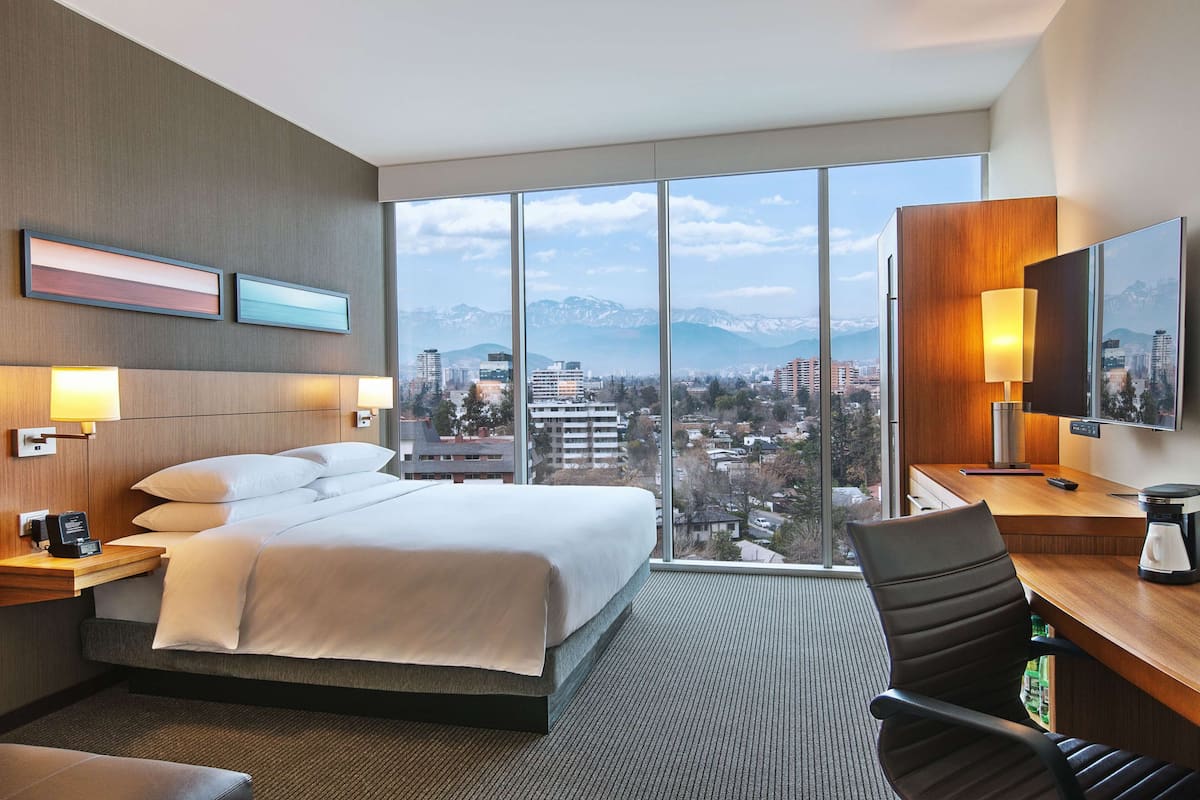 Ein Hotelzimmer mit einem großen Bett, einem Schreibtisch mit Stuhl, einer Kaffeemaschine und einem Fernseher.
