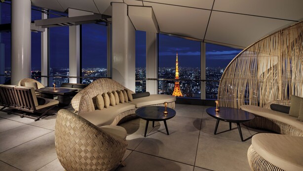 Een moderne lounge met panoramisch stadsgezicht, met een bank, stoelen en een ronde tafel.