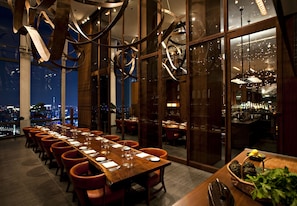 A dining area with a long table set for a meal, large windows offering a city view, and a modern chandelier. - Andaz Tokyo Toranomon Hills - a concept by Hyatt (Tokyo)