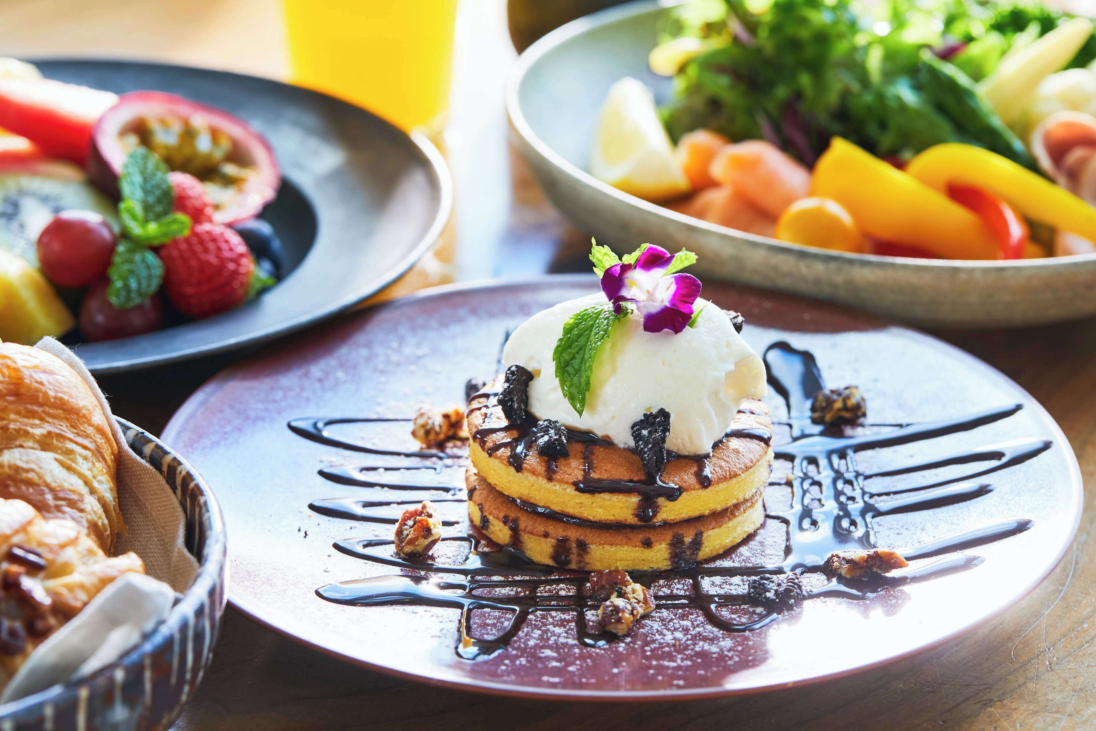 A breakfast setting with pancakes, fruit, and a bowl of salad.