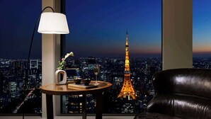 Een kamer met uitzicht op de Eiffeltoren 's nachts, een leren bank, een tafel met een lamp en een vaas met bloemen.