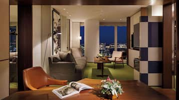 A modern living room with a wooden dining table, a sofa, and a coffee table. There is a view of the city at night through large windows.