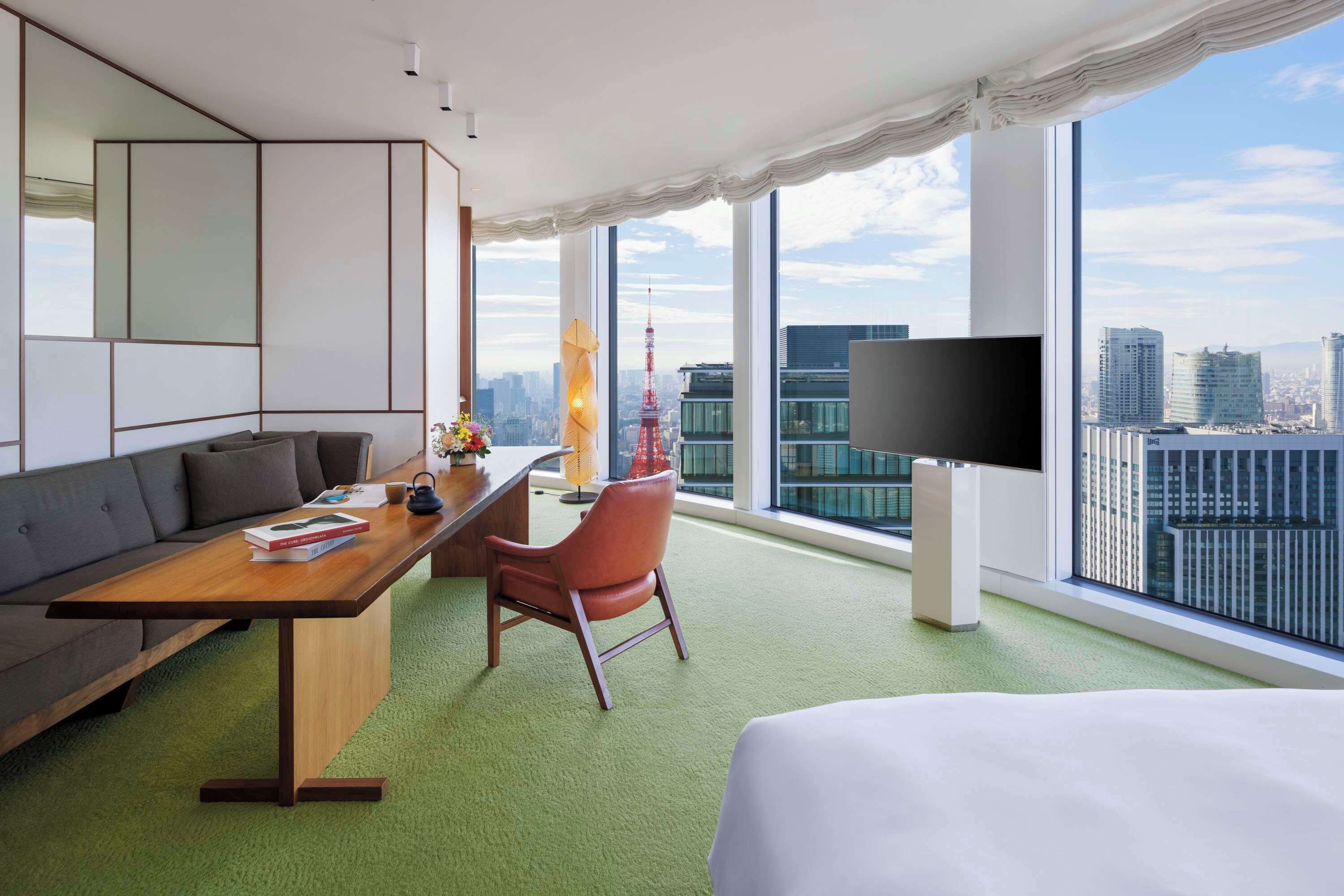 Ein Hotelzimmer mit einem großen Bett, einer Sitzecke, einem Schreibtisch mit Stuhl, einem Flachbildfernseher und Blick auf die Stadt.