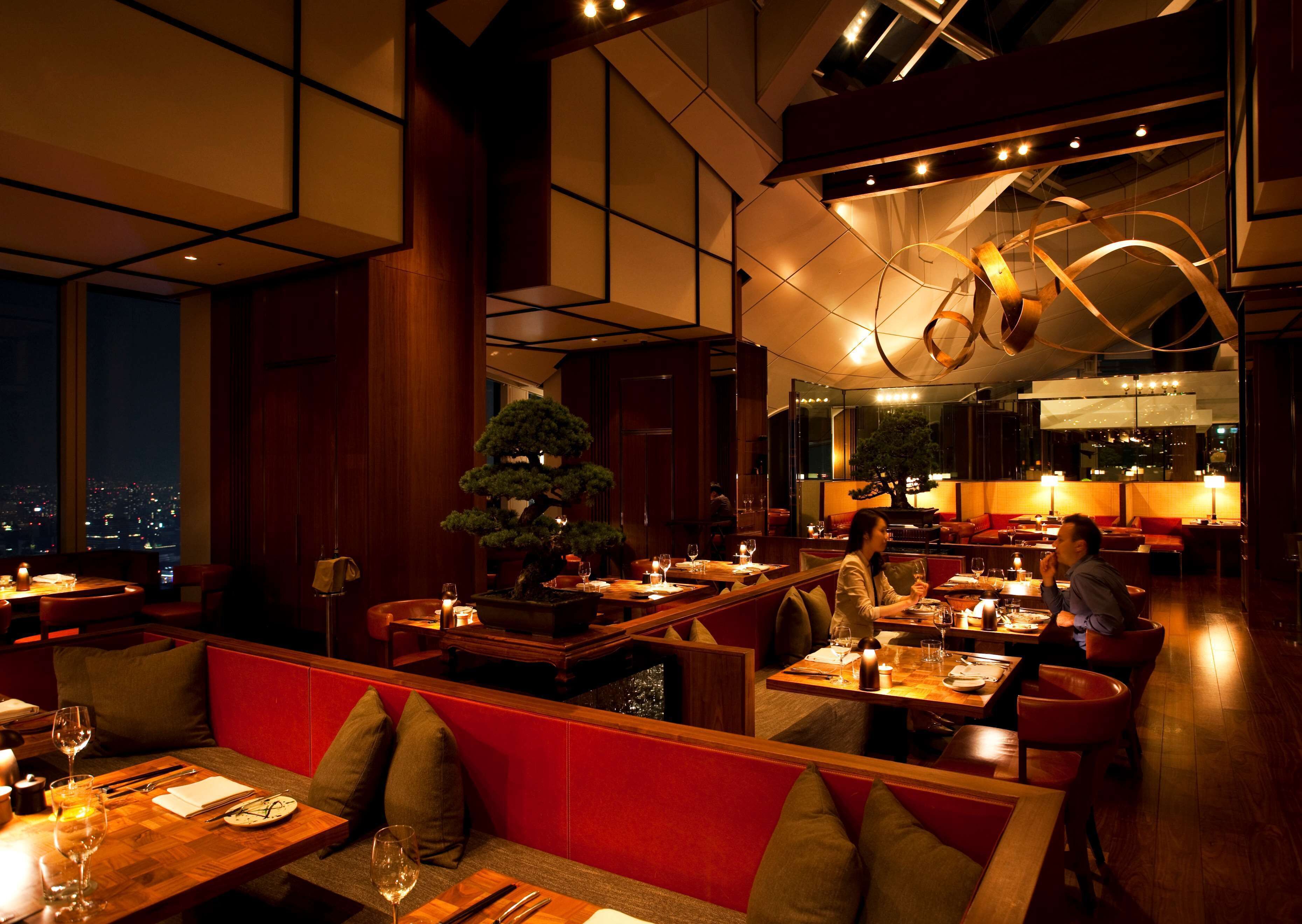 A modern restaurant with wooden furniture, red cushioned seating, and a bonsai tree centerpiece.