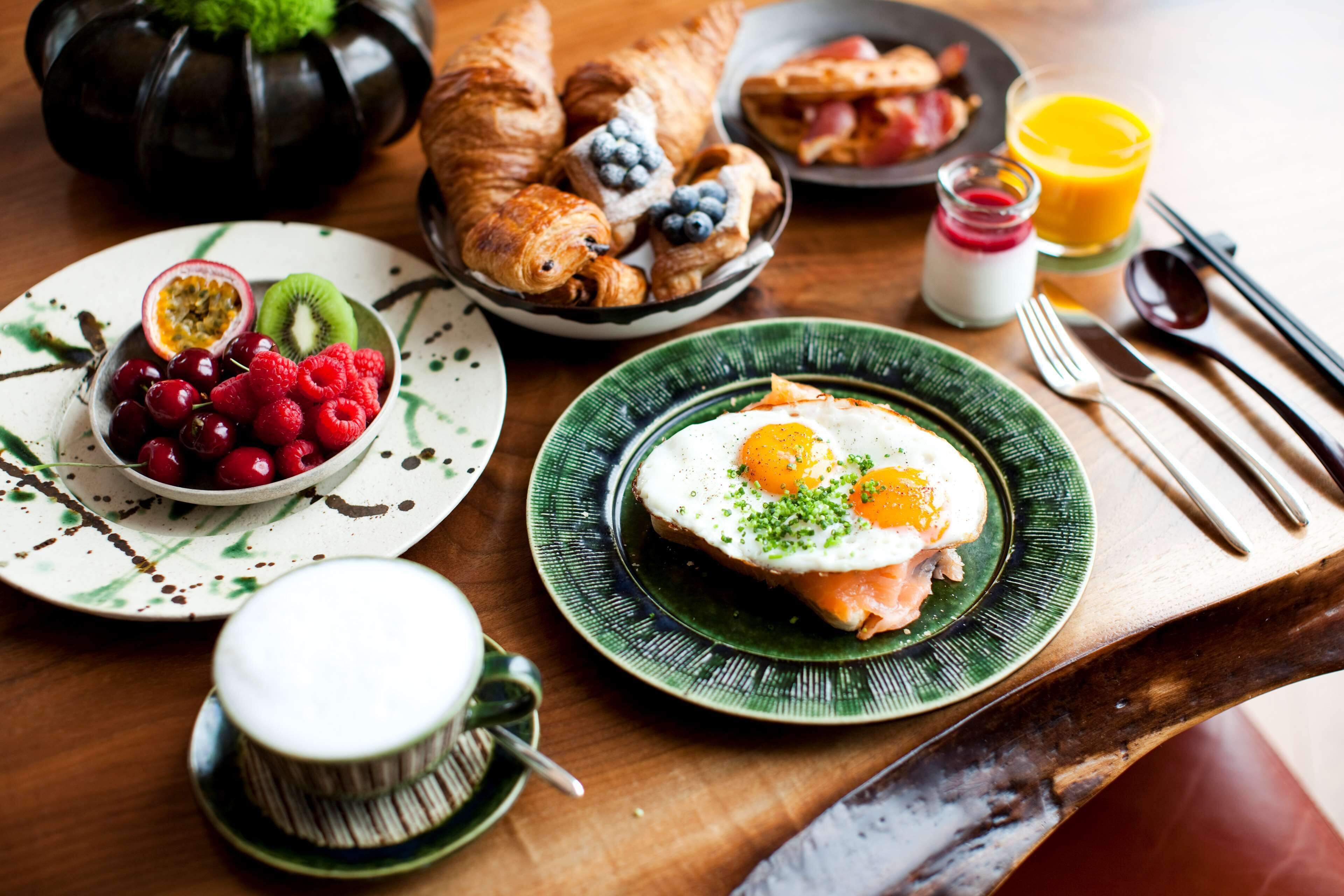 Ein Frühstückstisch mit Croissants, Obst, Eiern und einem Glas Orangensaft.