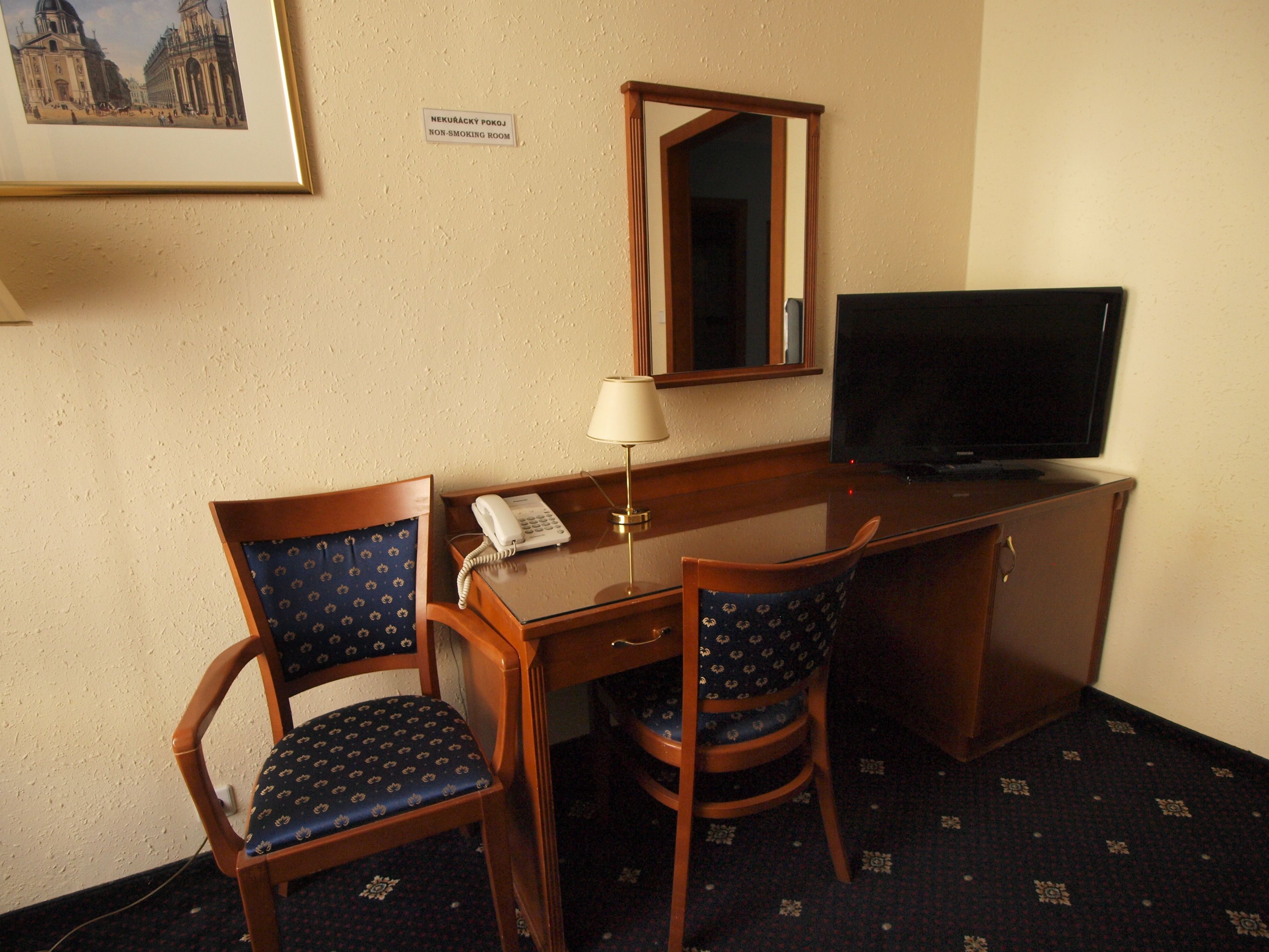 A hotel room with a desk, two chairs, a TV, a phone, and a non-smoking sign.