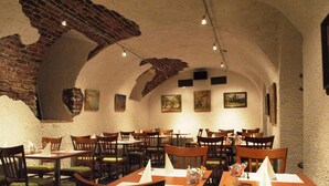 A restaurant with wooden tables and chairs, white tablecloths, and paintings on the walls. - Hotel Arbes (Prague)