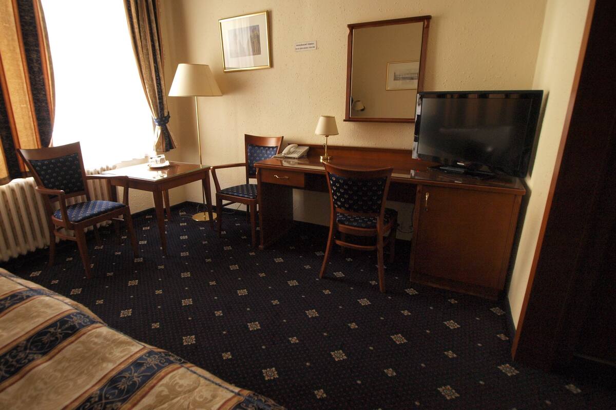 A hotel room with a bed, two chairs, a desk, a television, and a window with curtains.