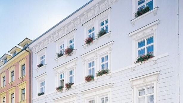 A multi-story hotel with white facades, arched windows, and flower boxes on the balconies. - Hotel Arbes (Prague)